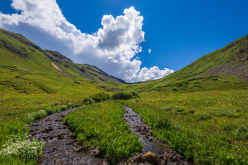 alpine stream in tundra meadow with big clouds and blue sky