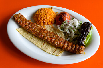 Grilled Turkish Adana, Urfa  Kebab with grilled vegetables, onion and rice on plate. Adana durum .
