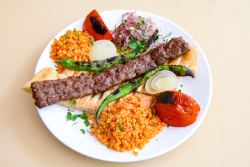 Grilled Turkish Adana, Urfa  Kebab with grilled vegetables, onion and rice on plate. Adana durum .