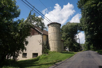 Fototapeta na wymiar Older Beige Silo and Frame House Partly Obscured by Trees
