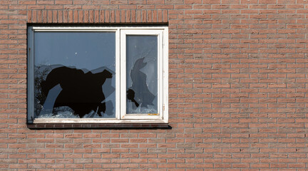 Broken glass window, probably due to vandalism, in a brick wall