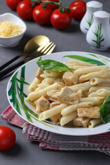 Penne pasta with chicken fillet and cheese in plate, served with cherry tomatoes on dark gray background, Vertical format