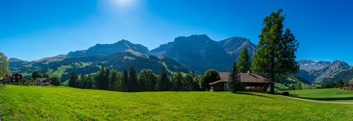 Obraz premium Adelboden im Panorama, Bergdorf mit vielen schönen und alten Holzhäusern, Bergwiesen, Wäldern und den hohen Bergen Grosser Lohner und Wildstrubel im Hintergrund. Streusiedlung im Engstligental. 