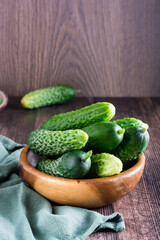 Fresh whole cucumbers in a bowl and on a wooden table. Diet organic food. Vertical view