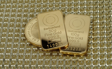 Fifty and one hundred gram gold bars and a 2 troy ounce gold coin on a textured golden background.
