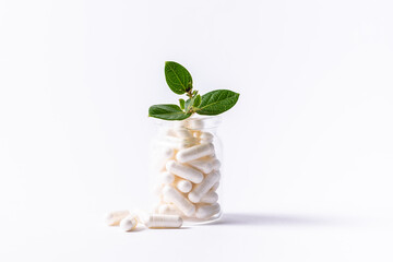 Natural herbal medicine concept. Glass jar with white medical capsules and green leaves on white background close up. Health care concept.