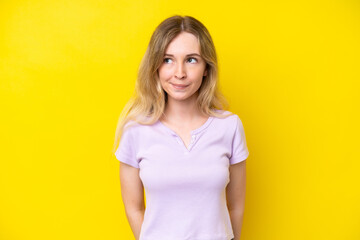 Fototapeta premium Blonde English young girl isolated on yellow background having doubts while looking up