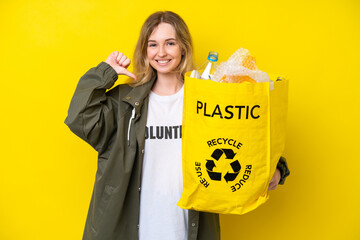 Blonde English young girl holding a bag full of plastic bottles to recycle isolated on yellow...