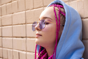 Portrait of a caucasian teenage hipster girl with pink braids and sunglasses using an earphones...