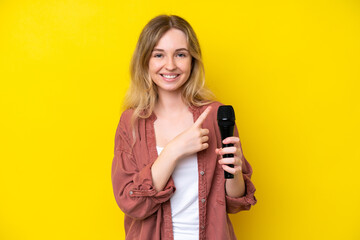 Young singer caucasian woman picking up a microphone isolated on yellow background pointing to the...