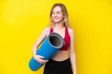 Young sport caucasian woman going to yoga classes while holding a mat isolated on yellow background looking to the side and smiling