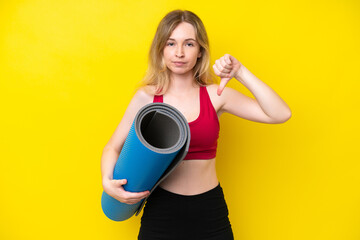 Young sport caucasian woman going to yoga classes while holding a mat isolated on yellow background showing thumb down with negative expression