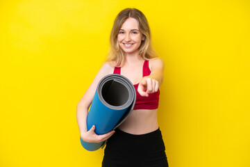 Young sport caucasian woman going to yoga classes while holding a mat isolated on yellow background pointing front with happy expression