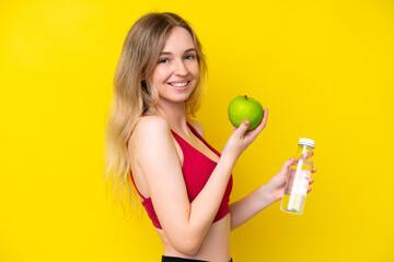 Blonde English young girl isolated on yellow background with an apple and with a bottle of water