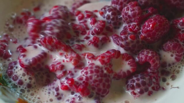 Fresh raspberries in milk are stirred with a spoon, making homemade yogurt from ripe berries.Close-up.Light breakfast of raspberries in milk. selective focus