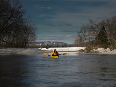 kayak surfer on an icy lake at the end of winter with view on Mont Tremblant peak in background, Quebec, Canada