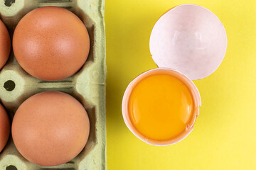 Pack of brown eggs with one broken open egg with raw yolk and shell on yellow background