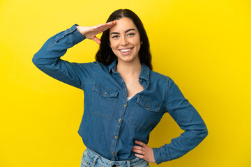 Young caucasian woman isolated on yellow background saluting with hand with happy expression