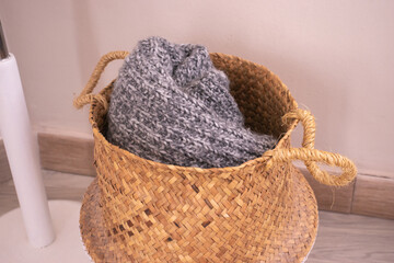 Warm grey knitted winter scarf of sweater in a brown wicker basket on the floor.