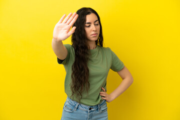 Young caucasian woman isolated on yellow background making stop gesture and disappointed