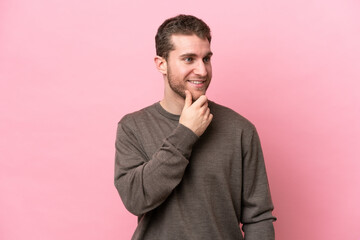 Young caucasian man isolated on pink background looking to the side and smiling