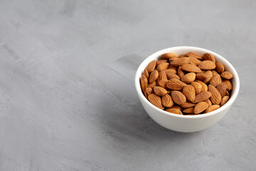 Raw brown almonds in a bowl on a gray background, low angle view. Copy space.