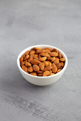 Raw brown almonds in a bowl on a gray background, low angle view.