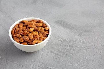 Raw brown almonds in a bowl on a gray background, low angle view.