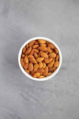 Raw brown almonds in a bowl on a gray background, top view. Flat lay, overhead, from above.