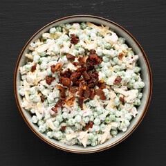 Homemade Creamy Bacon Pea Salad in a Bowl on a black surface, top view. Flat lay, overhead, from above.