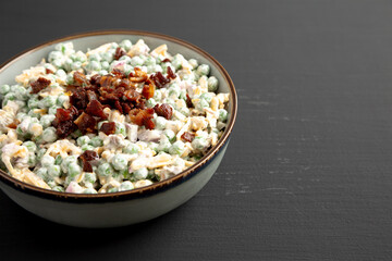 Homemade Creamy Bacon Pea Salad in a Bowl on a black background, side view. Space for text.