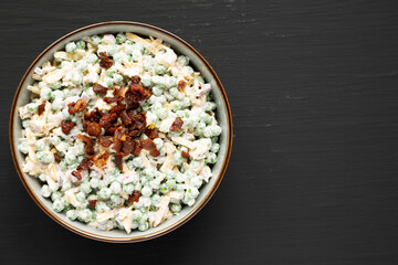 Homemade Creamy Bacon Pea Salad in a Bowl on a black surface, top view. Flat lay, overhead, from above. Copy space.