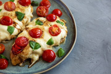 Homemade Caprese Chicken Parmesan with tomato, mozzarella and basil on a Plate, side view.
