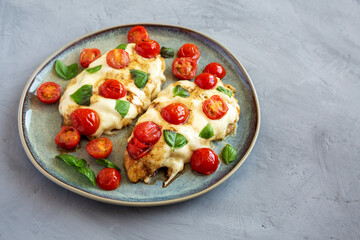 Homemade Caprese Chicken Parmesan with tomato, mozzarella and basil on a Plate, side view. Space for text.