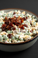 Homemade Creamy Bacon Pea Salad in a Bowl on a black background, side view. Close-up.