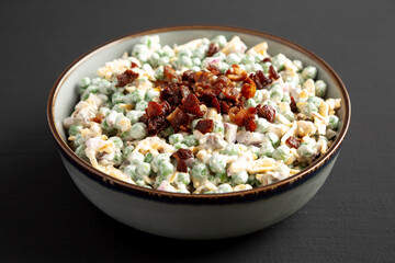 Homemade Creamy Bacon Pea Salad in a Bowl on a black background, side view.