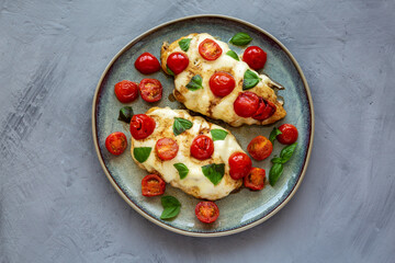 Homemade Caprese Chicken Parmesan with tomato, mozzarella and basil on a Plate, top view.