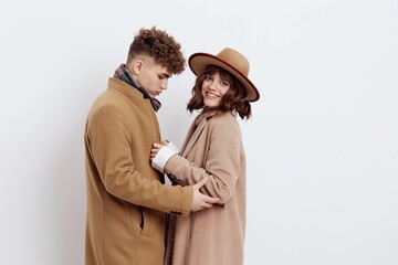 a cute couple stands on a light background dressed in coats and sweaters, a man stands against a woman and hugs her in front