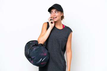 Young sport woman with sport bag isolated on white background keeping a conversation with the mobile phone with someone