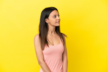 Young caucasian woman isolated on yellow background looking to the side