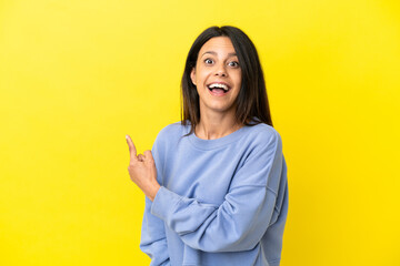 Young caucasian woman isolated on yellow background surprised and pointing side