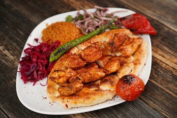 Grilled Turkish chicken wings served with pita, garnish,  onions, bulgur, roasted green pepper, and roasted tomato on white plate on wooden background. Served special restaurant presentation