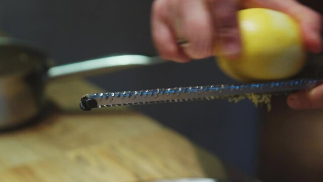 Chef grating lemon zest on grater on a cooked dish of baked fish