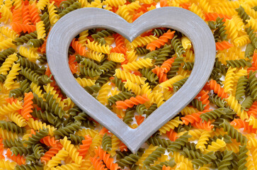 colorful uncooked fusilli pasta food background and heart shaped frame