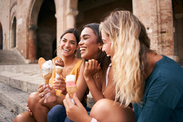 Three joyful young girl friends on a promenade smiling happily as they enjoy takeaway ice cream cones on summer vacation © CarlosBarquero