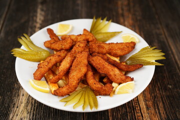 Crispy deep-fried chicken strips. Fried chicken strips on fried potatoes with pickles. Fried chicken and potatoes on a white plate on wooden background. 