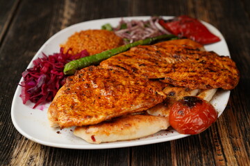 Grilled chicken breast. Fried chicken fillet with onions, bulgur, roasted green pepper, and roasted tomato on a white plate. Delicious Grilled chicken breast.