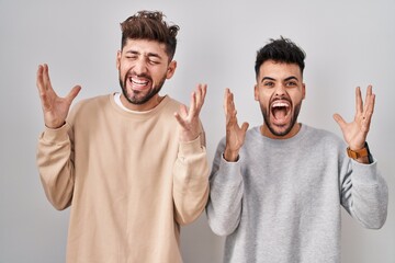 Young homosexual couple standing over white background celebrating mad and crazy for success with arms raised and closed eyes screaming excited. winner concept