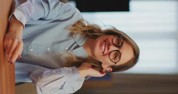 Female office worker wearing glasses smiling sitting at desk. Vertical video. Job interview, hr, employment concept