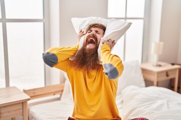 Young redhead man covering ears for noise at bedroom